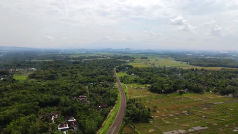 Aerial-backwards-shot-of-railway-lines-in-rural-area-of-Indonesia-with-many-plantation-fields