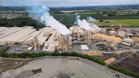 Aerial-of-wood-processing-manufacture,-smoking-chimneys,-industry-scene-from-New-Zealand