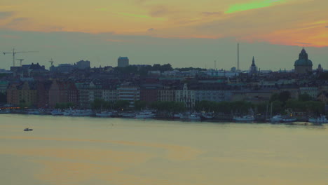 Aerial-shot-of-bay-in-Stockholm-with-view-of-moored-boats-and-buildings,-cranes-in-background