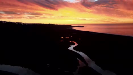 Spectacular-vivid-warm-coloured-sky-during-sunset-on-West-Coast,-South-Island,-New-Zealand---aerial-birds-eye