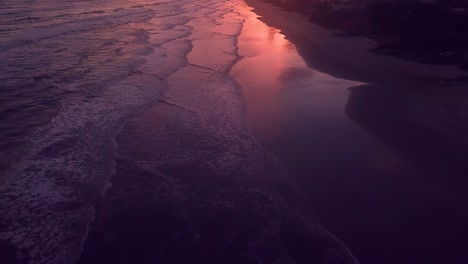 Flying-over-waves-in-Brazilian-beach-on-Atlantic-ocean-in-sunset,-beautiful-pink-skies-aerial-shot