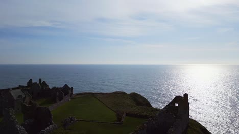 Aerial-journey-towards-and-over-magnificent-Dunnottar-Castle-in-Scotland-with-view-of-the-vast-ocean-stretching-beyond