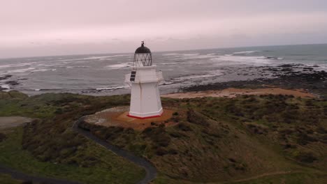 Waipapa-lighthouse-aerial-orbit-shot-at-wild-New-Zealand-coast-during-cold-cloudy-morning