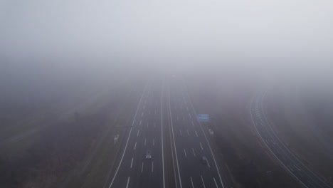 Aerial-backwards-flight-through-dense-clouds-above-German-highway-with-driving-cars-on-a-cloudy-day-during-autumn-season