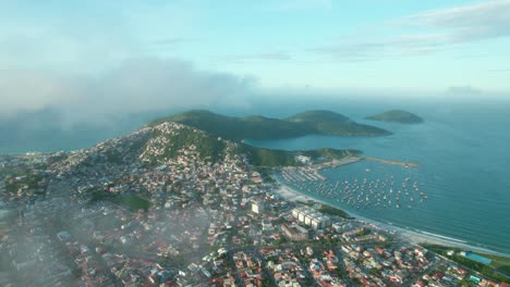 Panoramic-Aerial-View-of-Arraial-do-Cabo,-Dos-Anjos-and-Forno-Beach,-Blue-Skyline-and-Green-Hills-and-Clouds