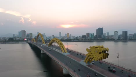 Colorful-aerial-of-iconic-Dragon-Bridge-Cau-Rong,-traffic-and-city-skyline-during-sunset-in-Danang,-Vietnam