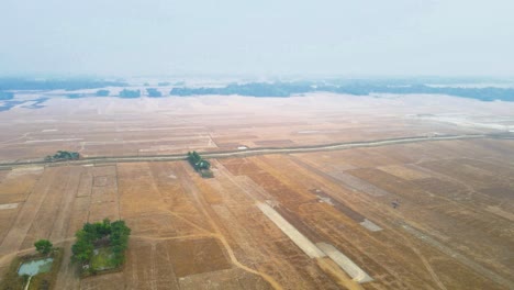 Drone-ascends-above-dry,-misty-farmland