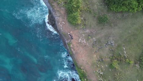 Descending-aerial-rotates-over-moto-tourist-on-steep-seaside-cliff