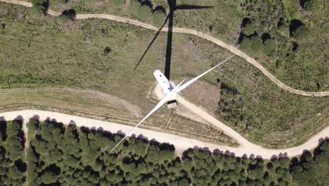 Aerial-top-down-view,-spinning-wind-turbine-on-a-green-field,-drone-orbit