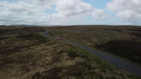 Front-view-of-red-car-travelling-along-a-countryside-single-track-road