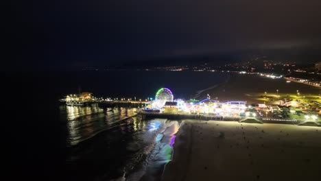 Santa-Monica-pier-at-night,-Pacific-Park-bright-light-attractions,-aerial-view