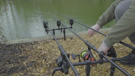 Close-up-shot-of-male-hands-setting-up-a-fishing-rod-and-spinning-reel-with-lake-water-in-the-background-at-daytime