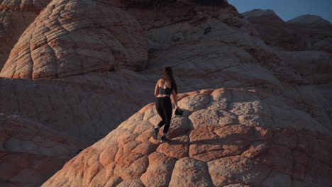 Young-Woman-With-Camera-Climbing-on-Unique-Sandstone-Formations,-Back-View