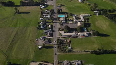 Traffic-on-main-road-to-Tapawera-small-town-in-New-Zealand---aerial-birds-eye-view,-houses,-public-and-commercial-buildings