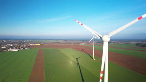Aerial-panorama-view-of-spinnging-windmills-on-rural-fields-and-village-in-background