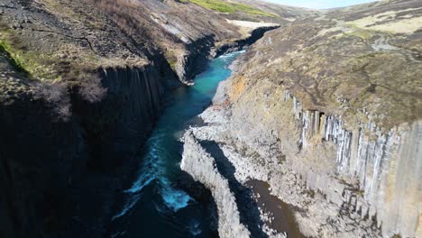 Egilsstadir,-Iceland:-Aerial-drone-fast-moving-shot-over-river-flowing-through-studlagil-canyon-into-basaltic-rock-formation-in-Iceland-at-daytime