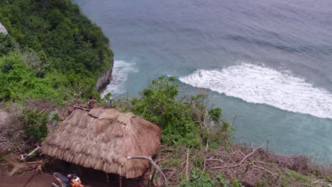 Small-local-hut-next-to-high-cliff-at-Sumba-island,-aerial-tilt-down