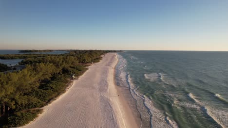 Drone-clip-moving-forward-along-golden-sandy-beach-with-forested-islands-and-waves-lapping-onto-the-shore