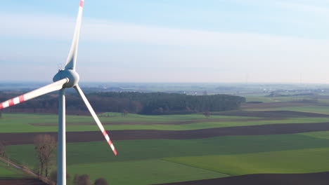 Aerial-close-up-of-spinning-Wind-Turbine-on-rural-field-with-forest-woodland-in-background