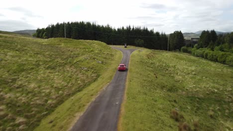 Red-vehicle-tracked-by-drone-from-rear-along-single-track-countryside-road