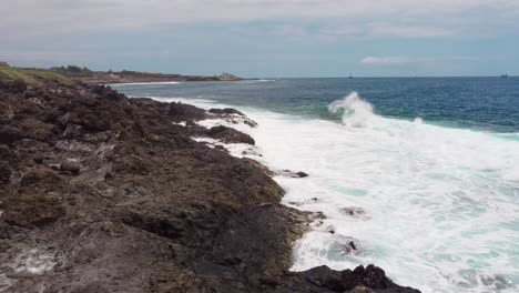 Powerful-waves-splashing-against-dark-volcanic-rock-in-Tenerife,-low-aerial