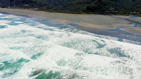 Olas-Blancas-De-Surf-Con-Hombre-Haciendo-Windsurf-En-La-Playa-De-Piha-En-Nueva-Zelanda