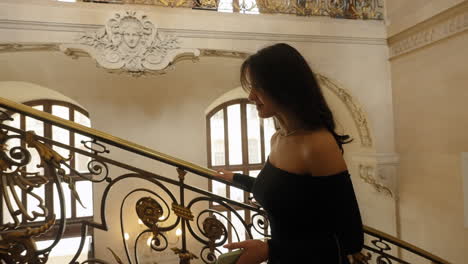 Beautiful-elegant-young-brunette-woman-wearing-a-black-dress,-climbing-a-Louvre-Museum-staircase