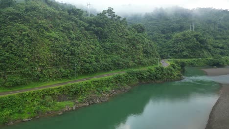Dichter-Wald-Auf-Bergen-Mit-Asphaltstraße-Und-Einem-Fluss-In-Catanduanes,-Philippinen