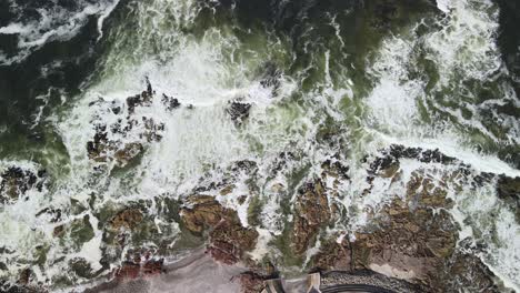 Birdseye-Aerial-View-of-Ocean-Waves-Breaking-on-a-Rocky-Coast-Making-Foam,-Drone-Shot-Top-Down-View