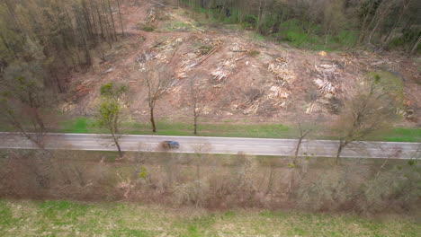 Aerial-top-down-shot-of-car-driving-on-road-beside-forest-after-deforestation