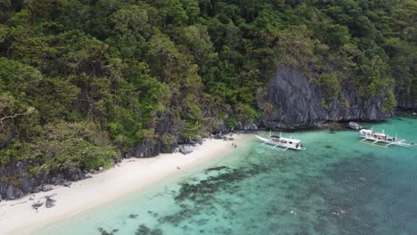 Island-hopping-Tour-Boats-with-People-snorkeling-at-Paradise-Beach-of-Cadlao-Island,-El-Nido