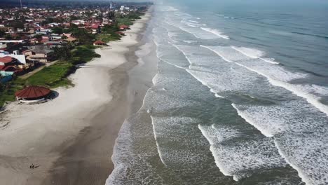 Tilting-aerial-shot-revealing-beach-and-ocean-in-summertime,-big-clouds-and-waves,-Itanhaem-Brazil