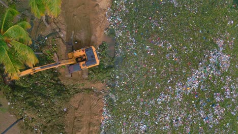 Excavator-digging-garbage-and-bottles-out-of-Caribbean-Sea-shoreline-at-playa-montesinos---environmental-Pollution-on-tropical-island-of-Dominican-Republic---aerial-straight-down