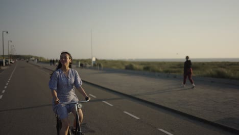Mujer-Guapa-Morena-En-Bicicleta-A-Lo-Largo-Del-Paseo-Marítimo-Frente-Al-Mar-Al-Atardecer