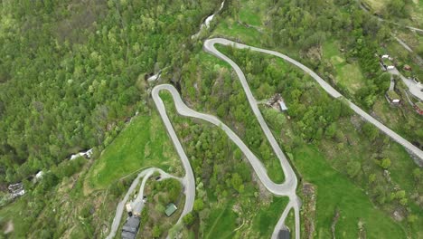 Winding-Geiranger-road-coming-down-from-the-mountains-and-to-the-village-of-Geiranger---Aerial-looking-down-at-winding-road-while-rotating-and-tilting-up-in-the-end