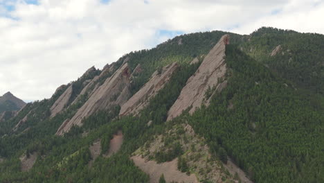 Close-up-aerial-view-of-warm-sun-hitting-Boulder-Colorado-Flatiron-mountains-above-Chautauqua-Park-with-full-green-pine-trees-and-blue-skies-with-clouds-on-a-beautiful-summer-day-for-hiking