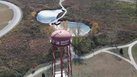 Aerial-orbit-of-Metro-Parks-watertowner-with-ponds-and-greenery,-Scioto-Audubon-Metro-Park,-Columbus,-Ohio