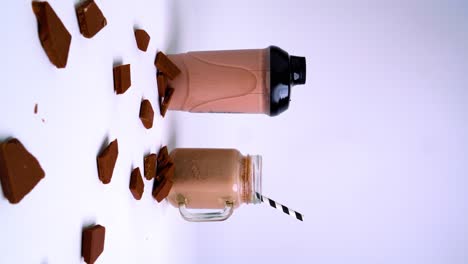 Toma-Vertical-De-Cámara-En-Movimiento-Con-Chispas-De-Chocolate,-Batido-De-Chocolate-Y-Paja-Rayada