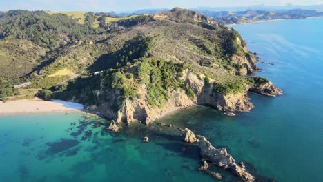 Rocky-cliff-with-forest-beside-the-beach-on-Coromandel-Peninsula-coast,-popular-destination-for-leisure-and-relax