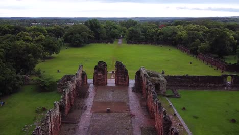 Drone-footage-tilting-down-onto-an-old-ruins-site-of-San-Ignacio,-Argentina-surrounded-by-a-luscious-green-environment