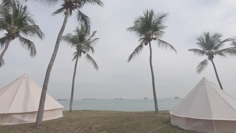 Two-tents-camping-on-the-palm-trees-beach-with-the-cargo-ships-from-far-away-in-the-sea-view