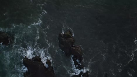 Aerial-view-flyover-of-white-waves-and-monochromatic-dark-ocean-rocks