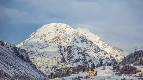 Small-building-on-foothill-of-massive-snowy-mountain,-time-lapse
