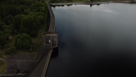 Orbital-footage-of-a-reservoir-dam-surrounded-by-trees,-grass-and-water