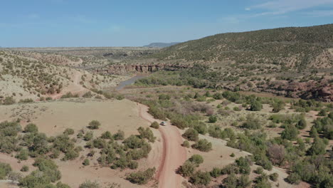 Scenic-aerial-follows-car-driving-through-desert-landscape-with-river