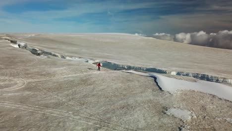 Aerial-view-of-a-climber-walking-towards-the-edge-of-an-ice-crevasse,-cracked-on-the-ice-surface-of-an-icelandic-glacier