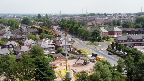 Tall-crane-setting-building-foundation-in-British-town-neighbourhood-aerial-descending-orbit-view-above-suburban-townhouse-rooftops