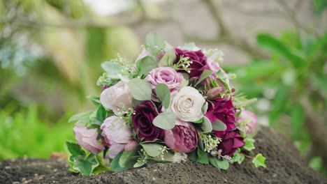 A-beautiful-wedding-bouquet-of-mixed-flowers-laying-on-a-stone-surface-outdoors