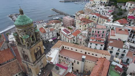 Stunning-architecture,-clock-tower,-and-city-square-market-in-Amalfi-Italy,-aerial