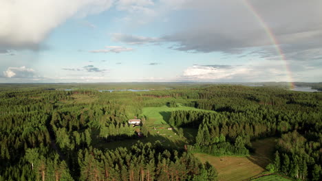 Stunning-Rainbow-over-Beautiful-Serene-Forest-and-Lake-Landscape-in-Finland,-Farm-Houses-in-the-Foreground,-Near-Kuopio